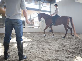 Female horseback riding with instructor in indoor paddock