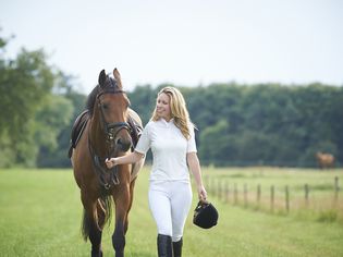 Female jockey walking horse in paddock.