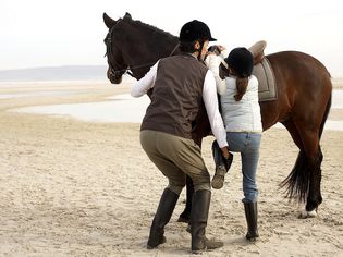 Woman helping child mount horse